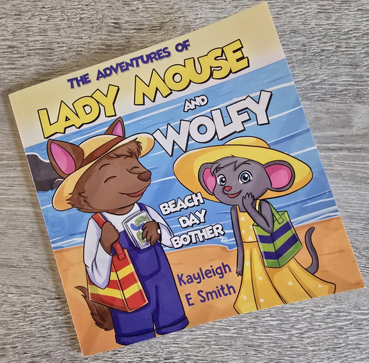 Cover of the children's book The Adventures of Lady Mouse and Wolfy featuring cartoon mouse and wolf characters at the beach with hats and bags.